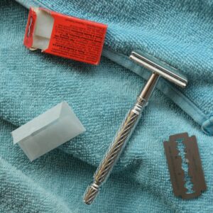 Close-up of a vintage razor, blade, and packaging on a blue towel.