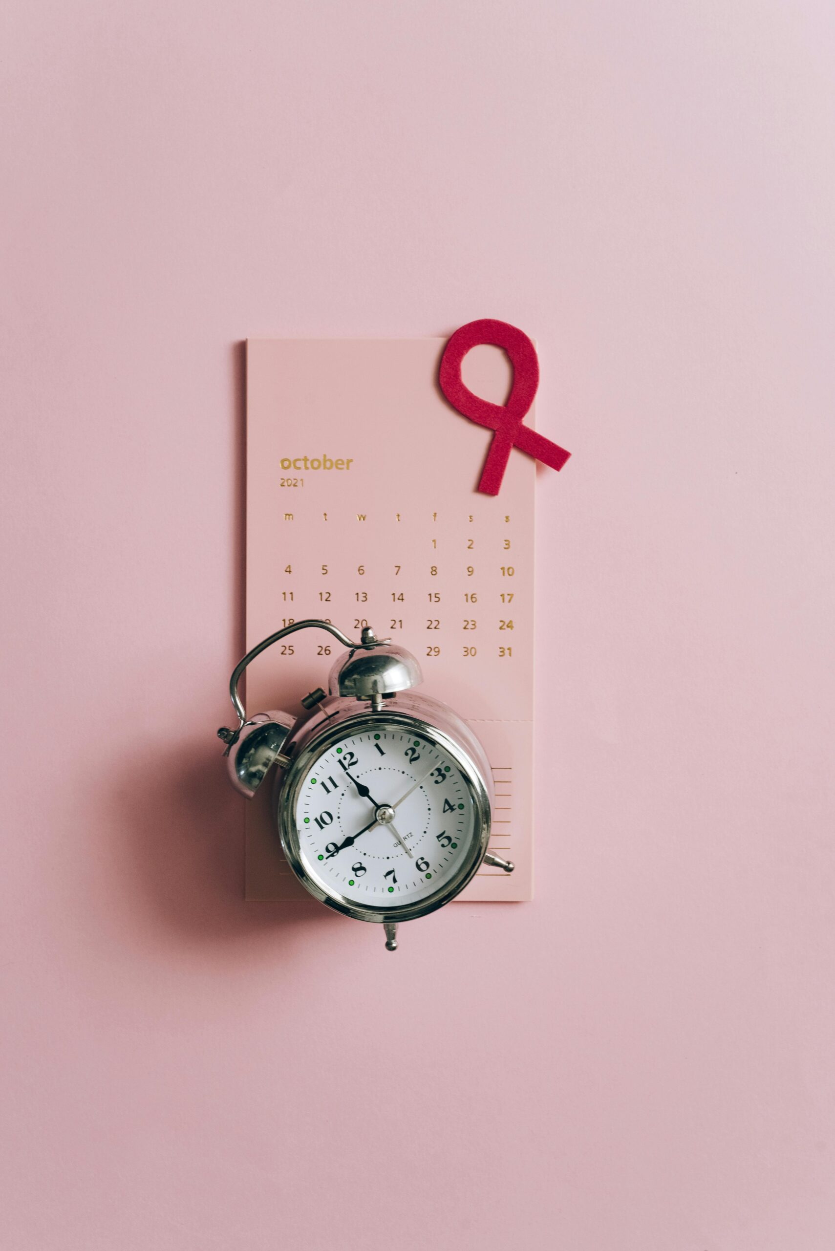 Conceptual image of a clock with a pink ribbon and October calendar for breast cancer awareness.