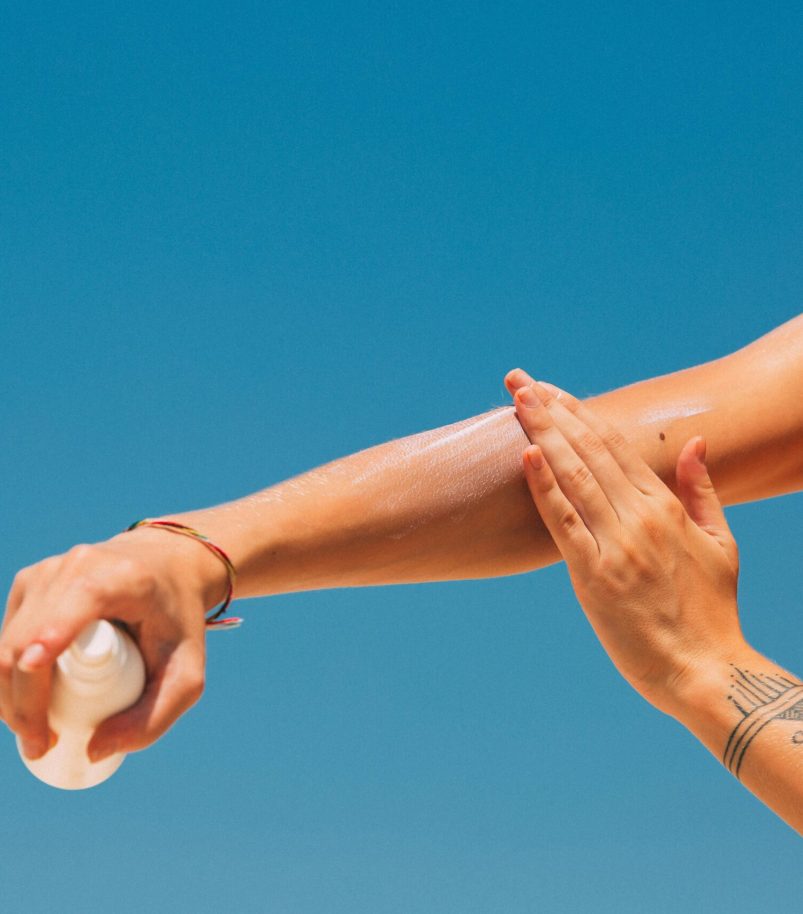 pexels-photo-8157145-8157145 Close-up of a woman applying sunscreen on her arm under a clear blue sky at the beach.